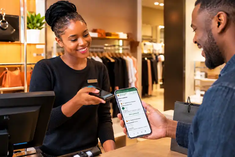 Two people at a retail counter, one holding a phone showing a loyalty card.